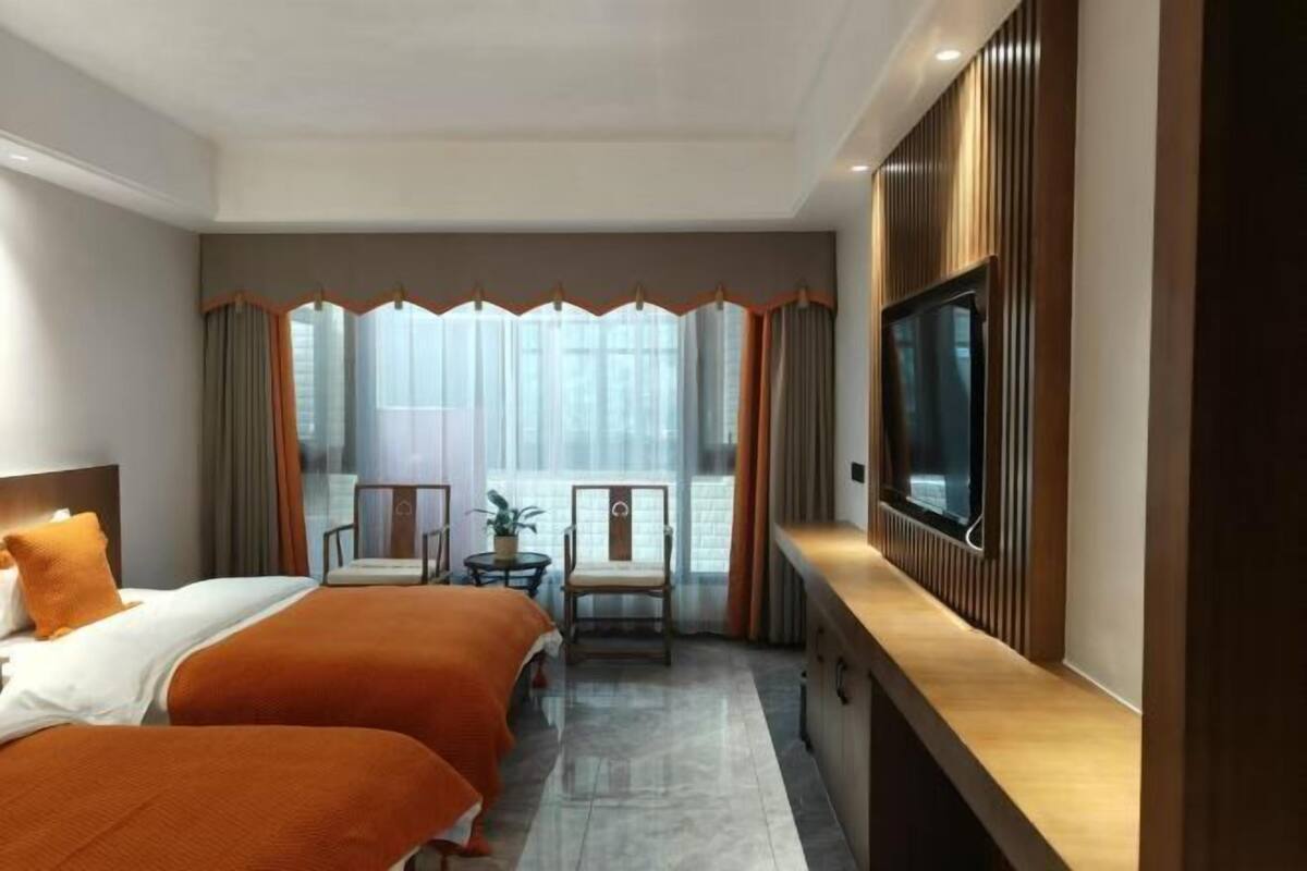 A hotel room with two beds, a TV, a balcony with a chair, and a view of the city.