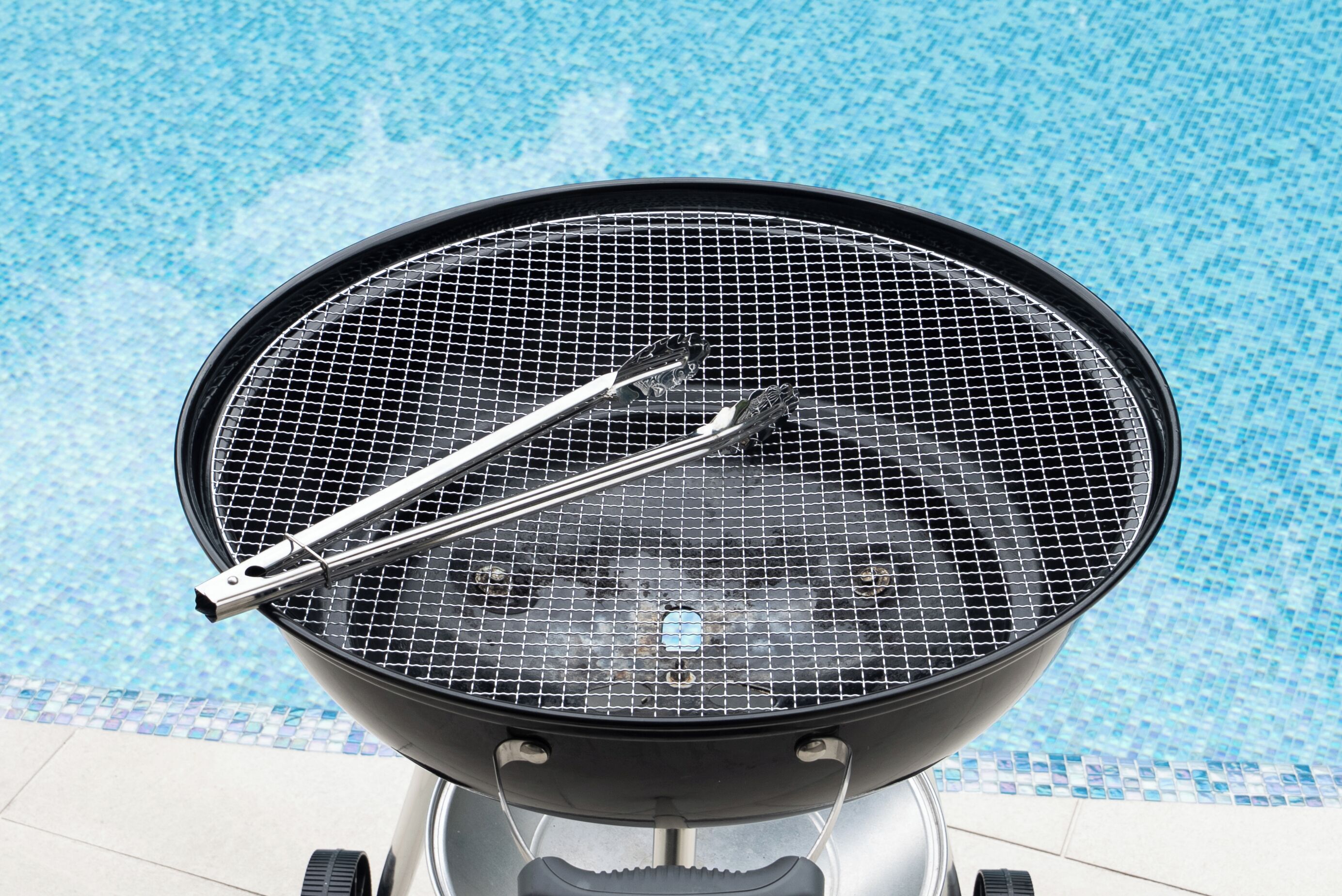 Una griglia circolare con piano a rete, situata vicino a una zona piscina piastrellata.