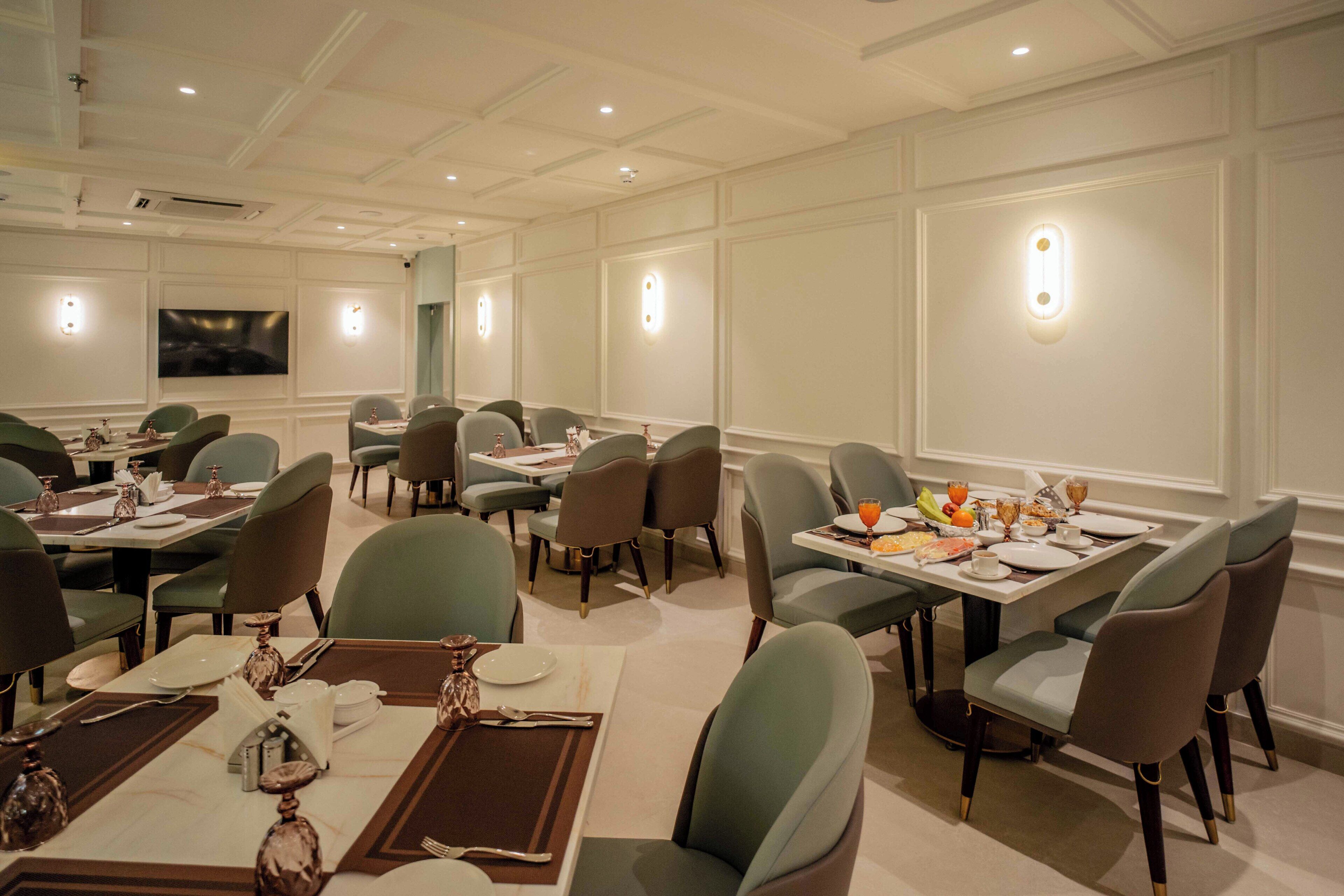 A dining area with tables set for meals, chairs, and a television screen on the wall.