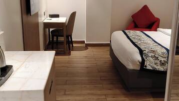 Quarto de hotel com cama, escrivaninha, cadeira e chão de madeira.