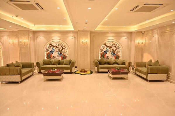 A spacious room with three sofas arranged in a U-shape, a coffee table in the center, and decorative wall art featuring peacocks. - Arth Boutique Hotel (Kota)