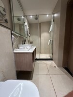Un baño moderno con ducha envuelta en vidrio, un lavabo blanco y un espejo.