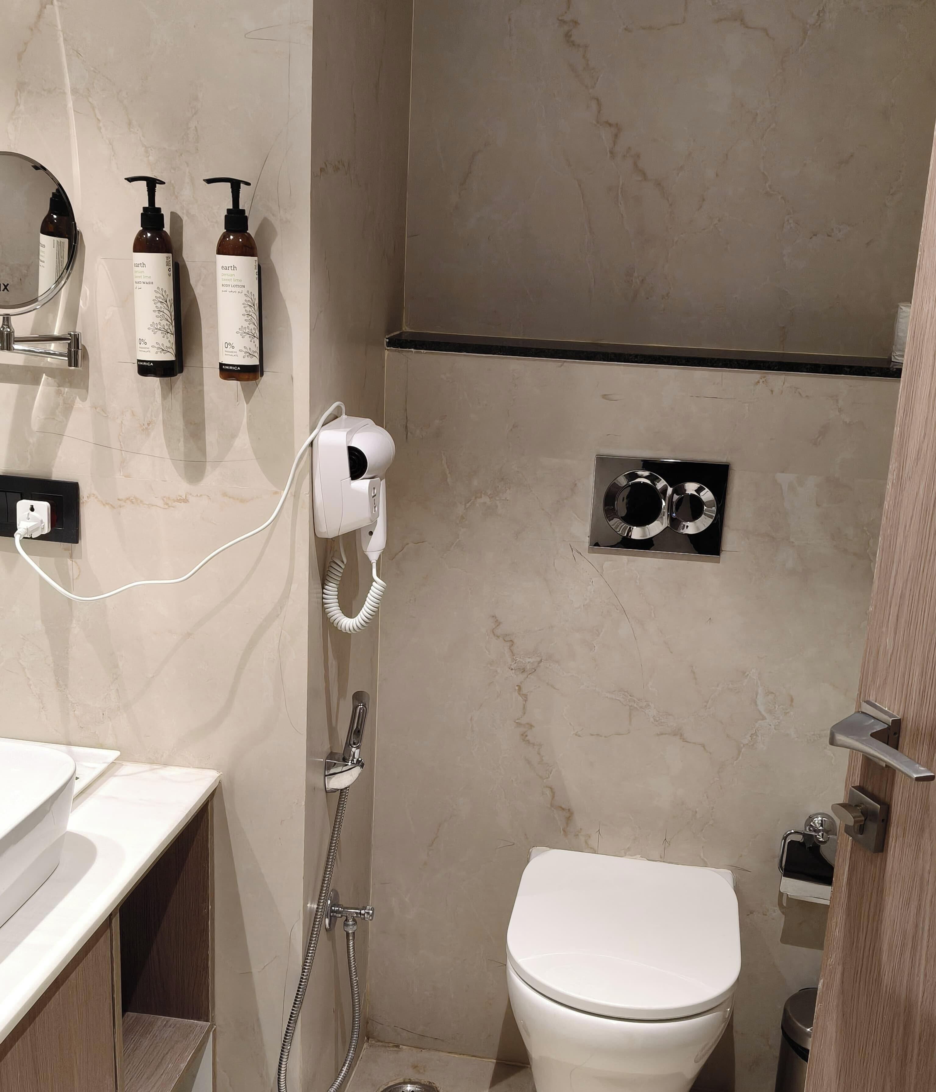 A bathroom with a toilet, a shower, a hairdryer, and two bottles of body lotion.