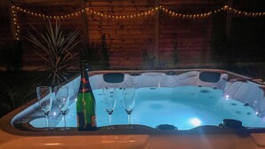 A hot tub with a bottle and glasses, surrounded by string lights. - La Maison Palulova - Jacuzzi - 400m from the beach (Plouescat)
