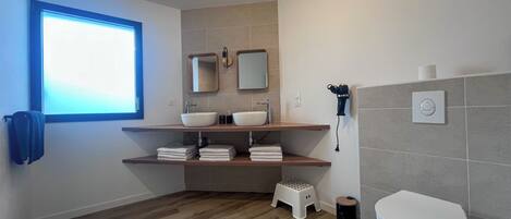 A modern bathroom with a window, two sinks, a toilet, and a hairdryer.