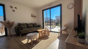 A modern living room with a sofa, ottoman, coffee table, and a TV. - La Maison Palulova - Jacuzzi - 400m from the beach (Plouescat)
