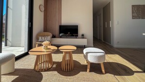 A modern living room with a TV, sofa, two wooden tables, and a large window. - La Maison Palulova - Jacuzzi - 400m from the beach (Plouescat)