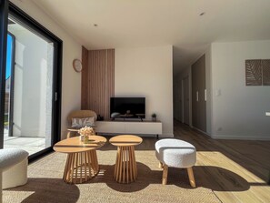 A modern living room with a TV, sofa, two wooden tables, and a large window.