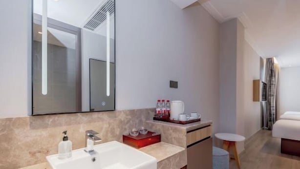 A modern bathroom with a large mirror, a sink, and a small table with toiletries. - Homeinn (Yangzhou)