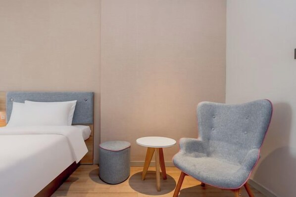 A modern hotel room with a bed, a grey armchair, and two small tables. - Homeinn (Yangzhou)