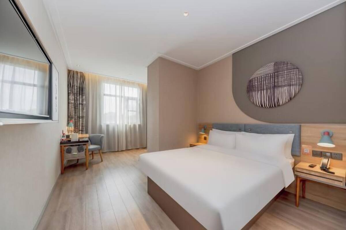 A hotel room with a bed, bedside table, lamp, and a wall-mounted artwork.