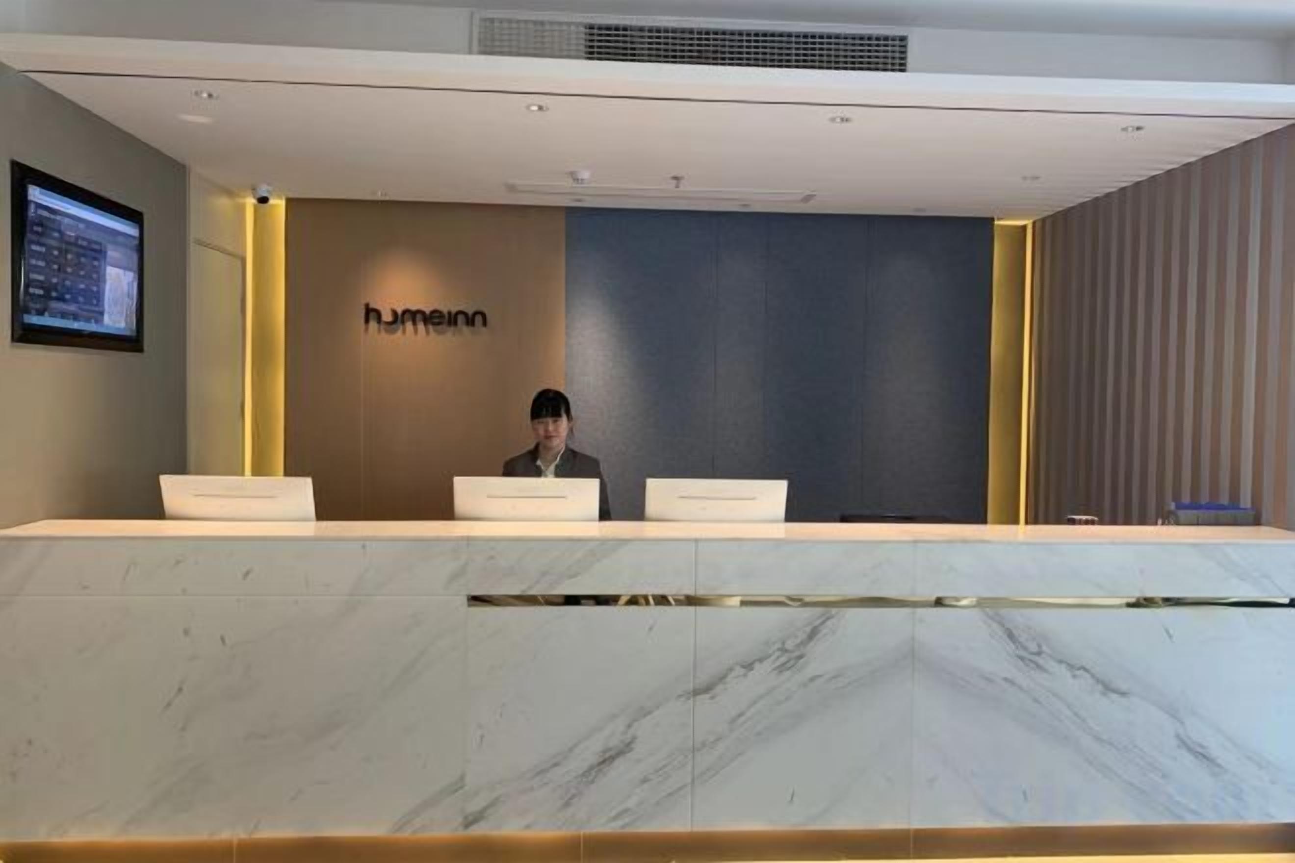 Un mostrador de recepción con encimera de mármol, una persona sentada detrás y un letrero con la palabra 'humeinn' en la pared.