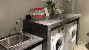 A compact laundry area with a washing machine, a sink, and a countertop with bottled water and a basket. - Homeinn (Yangzhou)