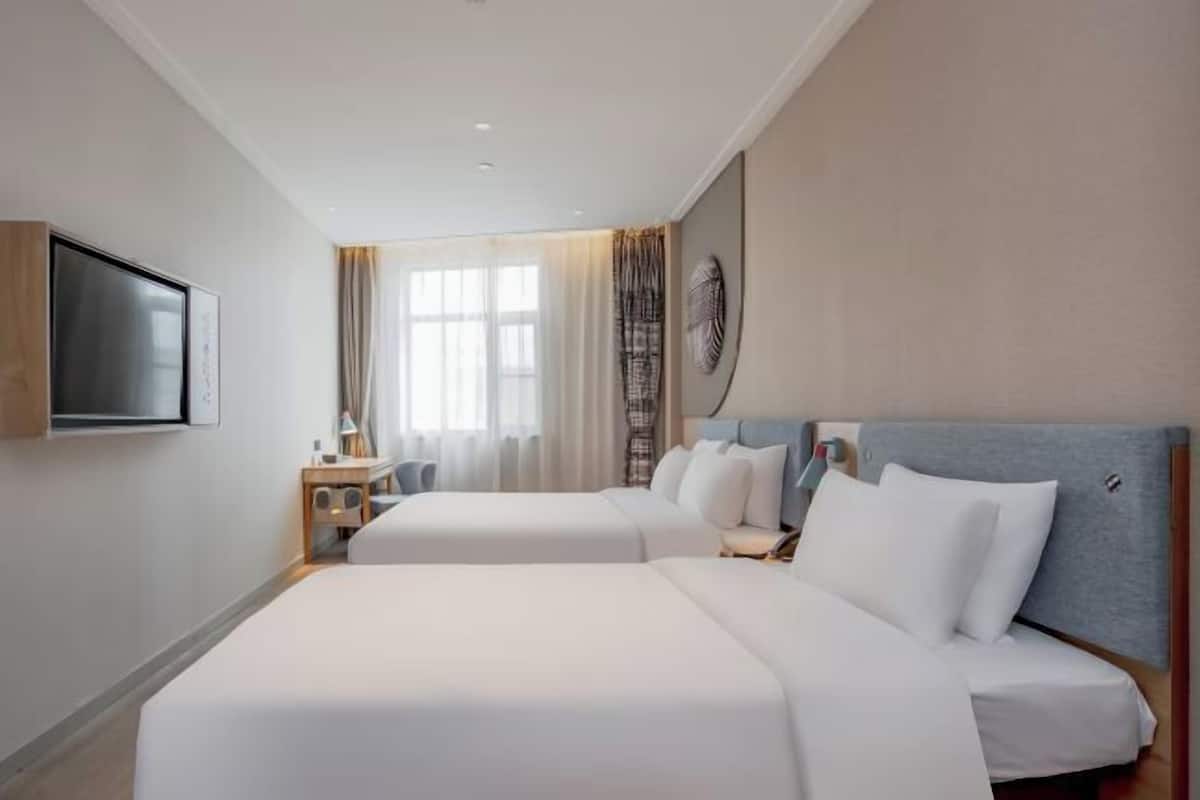 A hotel room with two beds, a flat-screen TV, a desk, and a window with curtains.