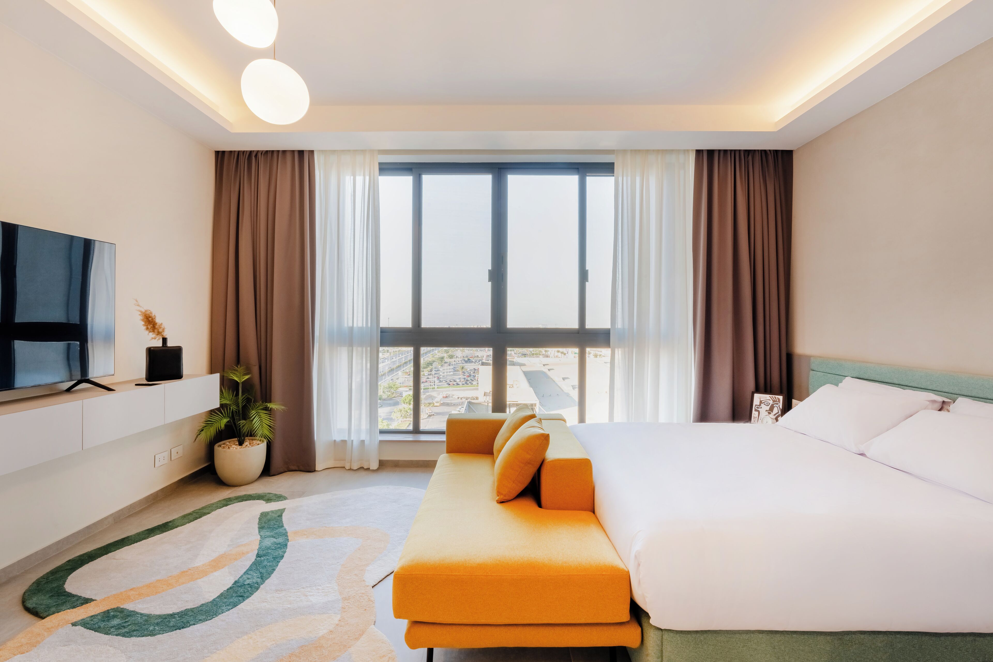 Een hotelkamer met een groot bed, een bank, een televisie en een raam met gordijnen.