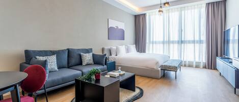 A modern hotel room with a sofa, a bed, a dining table, and a TV.