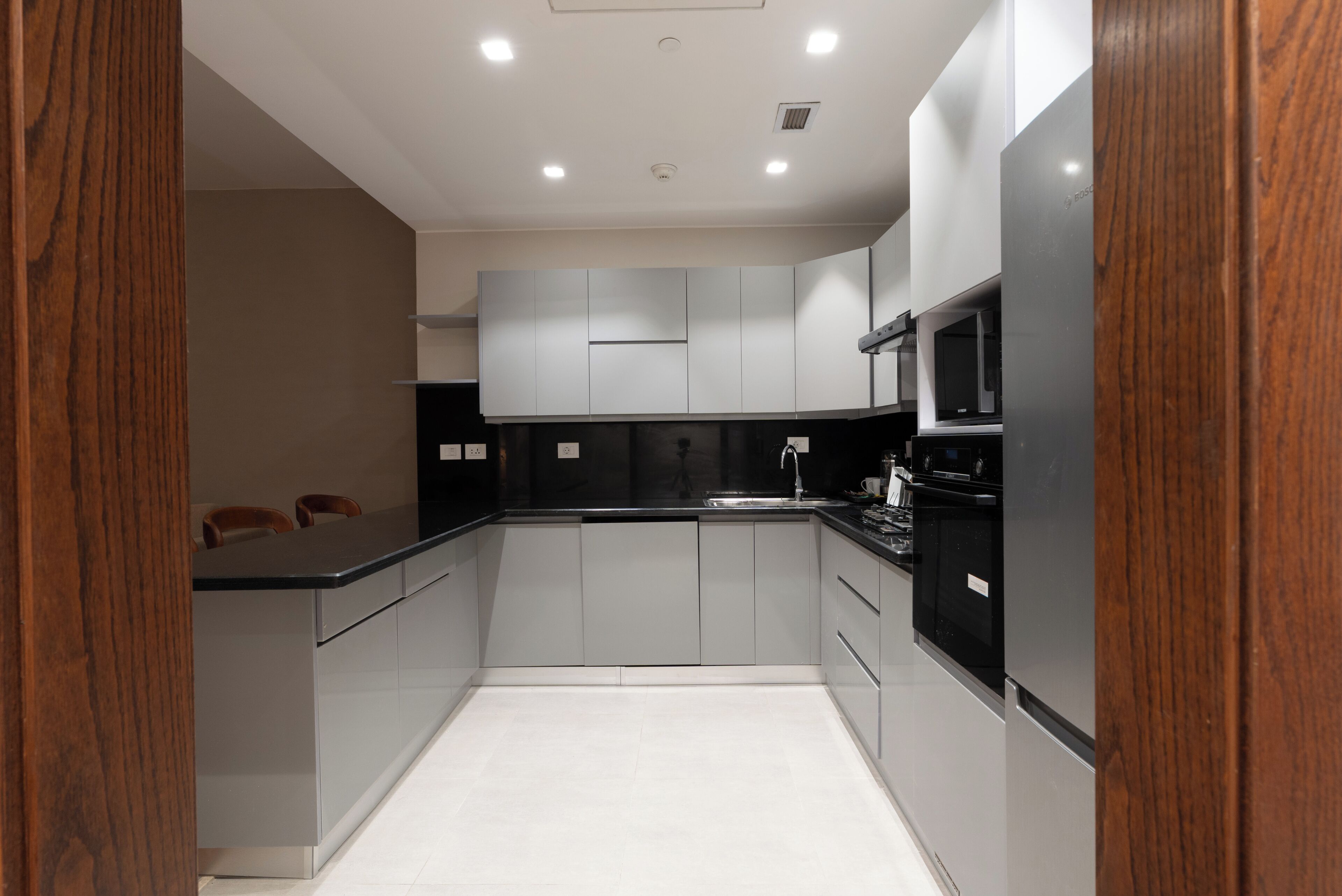 A modern kitchen with grey cabinets, a black countertop, and a stainless steel sink.