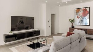 Una sala de estar moderna con una televisión de pantalla plana, un sofá, una mesa de centro y un cuadro en la pared.