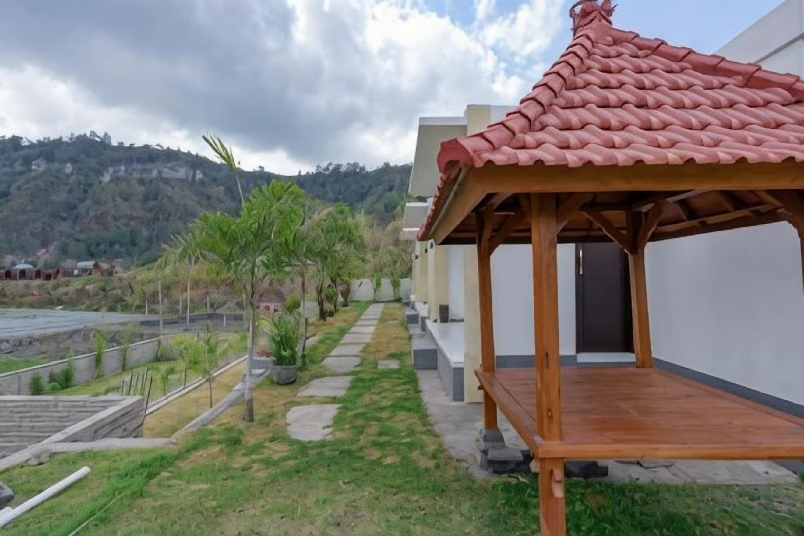 A covered outdoor area with a wooden structure, a paved pathway, and a view of a hilly landscape.