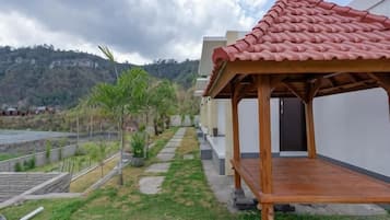 A covered outdoor area with a wooden structure, a paved pathway, and a view of a hilly landscape.