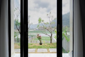 A view through a glass door with a potted plant and a small garden area. - Batur Kencana Villa Mitra RedDoorz (Bali)