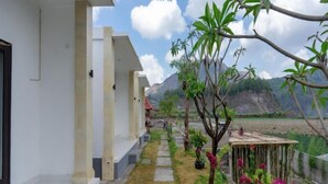 A building with a pathway leading to a covered area, surrounded by greenery and a mountainous backdrop. - Batur Kencana Villa Mitra RedDoorz (Bali)