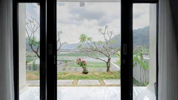 A view through a glass door with a potted plant and a landscape with trees and mountains.