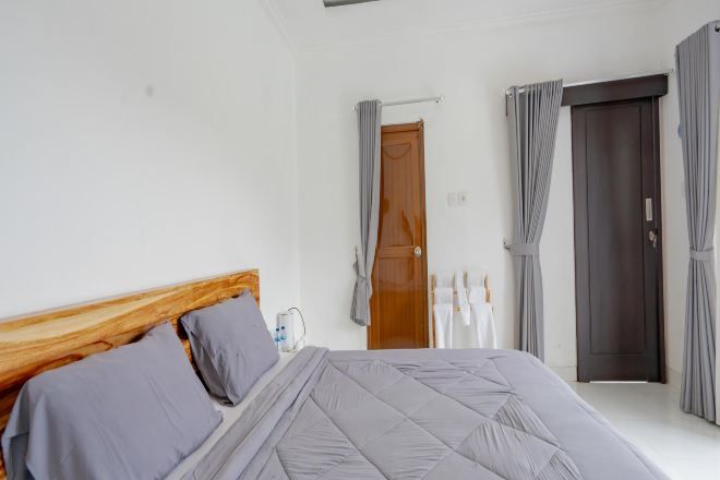 A bedroom with a wooden headboard, a bed with grey bedding, a wooden door, and grey curtains.