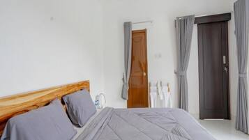 A bedroom with a wooden headboard, a bed with grey bedding, a wooden door, and grey curtains.