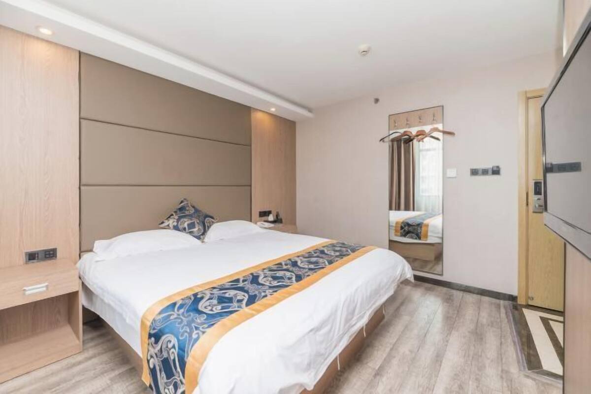 Una habitación de hotel moderna con una cama grande, una mesita de noche, un espejo y un armario.