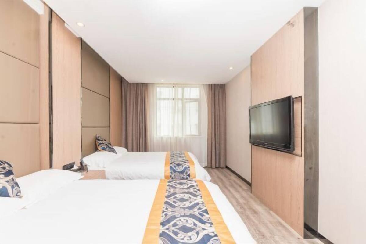 Habitación de hotel con dos camas, un televisor montado en la pared y una ventana con cortinas.