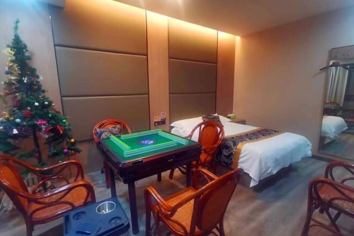 Una habitación de hotel con cama, una mesita con un juego de mesa verde, un árbol de Navidad y un espejo.