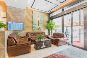 Een hotellobby met leren banken, een bijzettafeltje, een digitaal scherm en een groot raam.