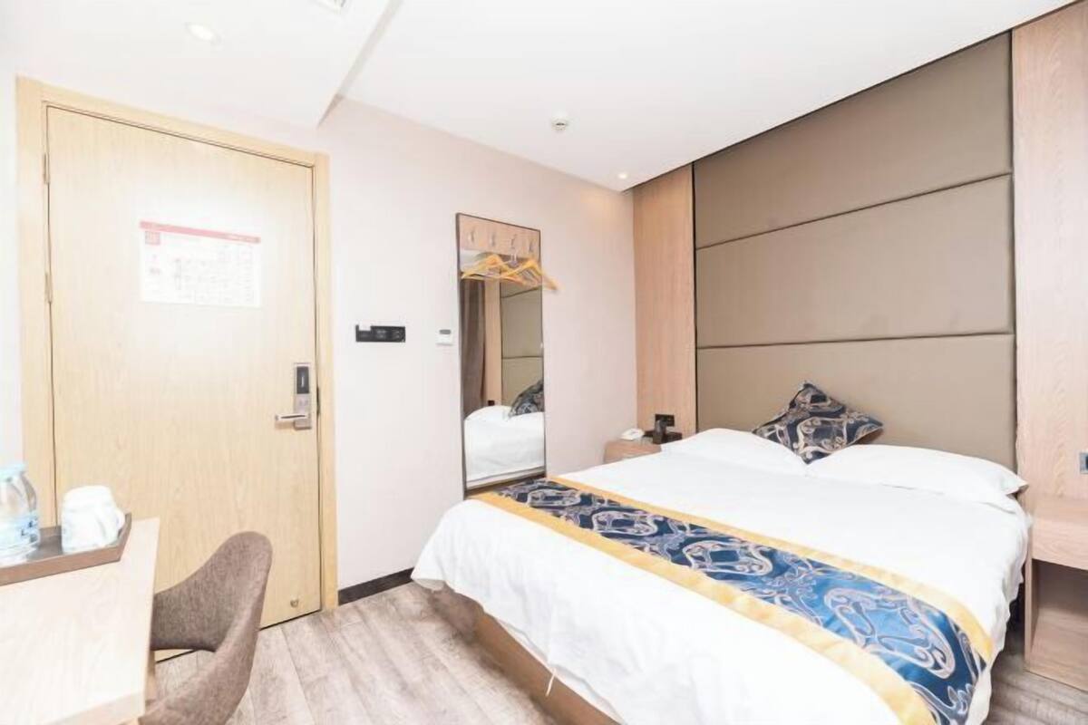 Una habitación de hotel con una cama, un escritorio con una silla, un espejo y una puerta.