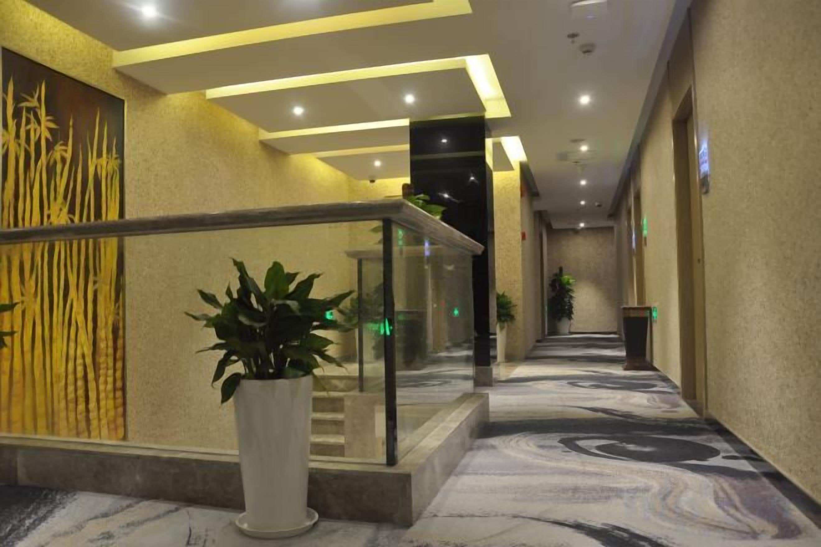 A hotel corridor with a marble floor, a glass railing, and potted plants.