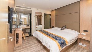 Habitación de hotel con cama, escritorio, televisor, espejo y zona de ducha.