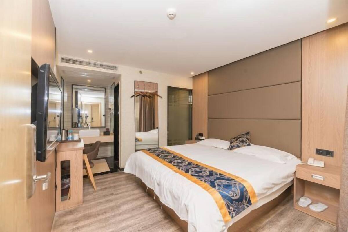 Habitación de hotel con cama, escritorio, televisor, espejo y zona de ducha.