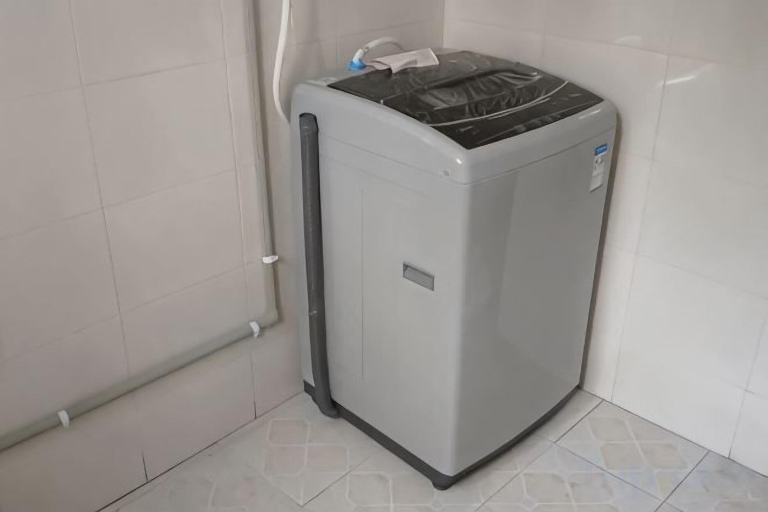 A compact, grey, wall-mounted laundry machine in a corner with a visible control panel and a small label on the side.