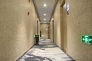 Un pasillo de hotel con alfombra estampada, paredes con letreros de salida de emergencia y una puerta al final.