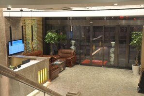 Eine Lobby mit Empfangsschalter, Ledersitzgelegenheiten, einer großen Pflanze und einer Treppe.