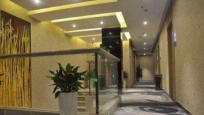 Un pasillo de hotel con piso de mármol, barandilla de vidrio y plantas en macetas.