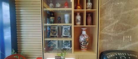 A room with a wooden slatted wall, a glass display case with decorative items, a table with a vase, and a chair.