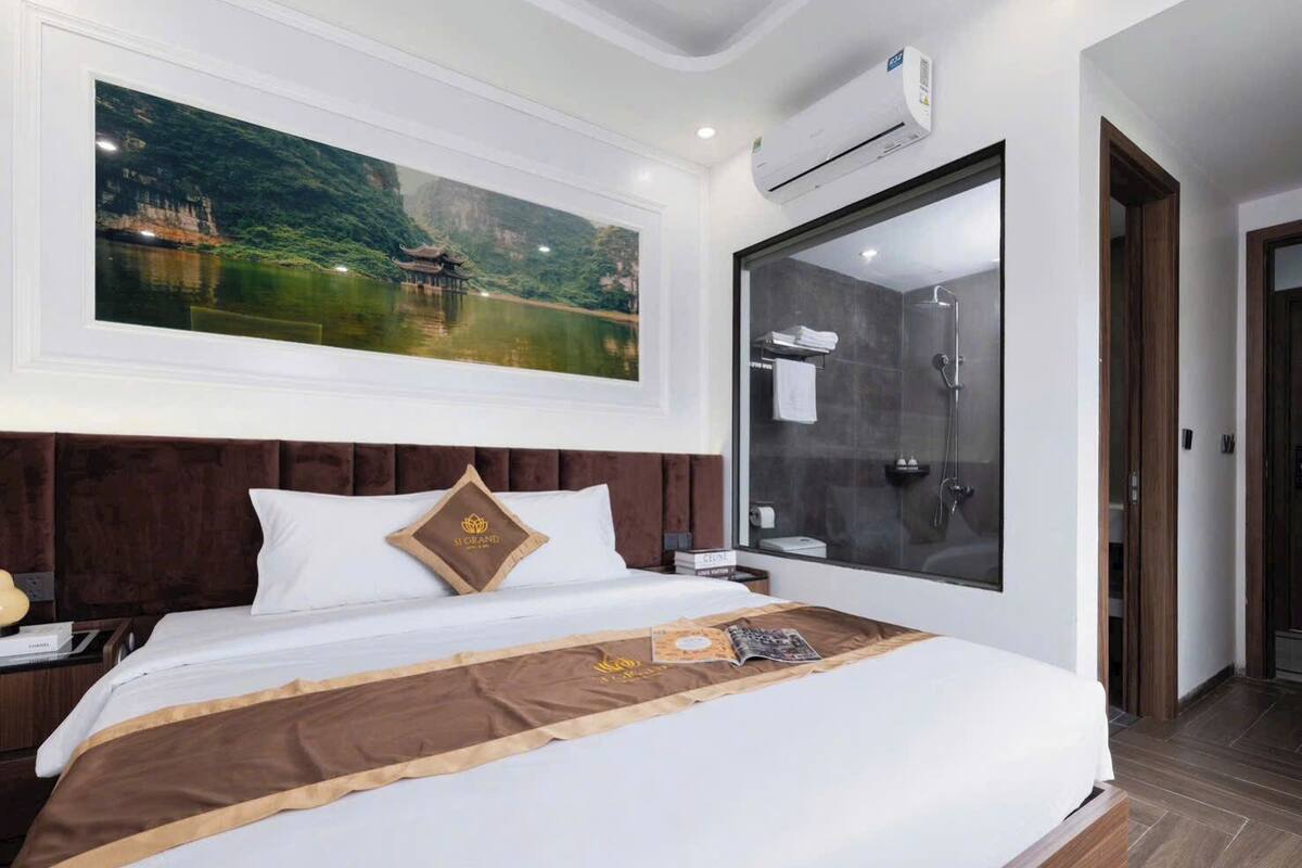 Habitación de hotel con una cama grande, un cuadro de un edificio tradicional, una ducha moderna y un ventanal amplio.