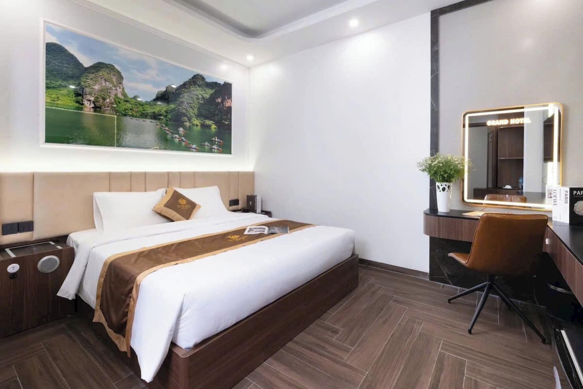 Una habitación de hotel moderna con una cama grande, un escritorio con espejo y una vista panorámica de un paisaje montañoso.