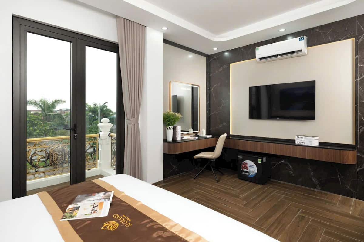 Una habitación de hotel moderna con una cama grande, un escritorio con silla, un televisor y un equipo de aire acondicionado.