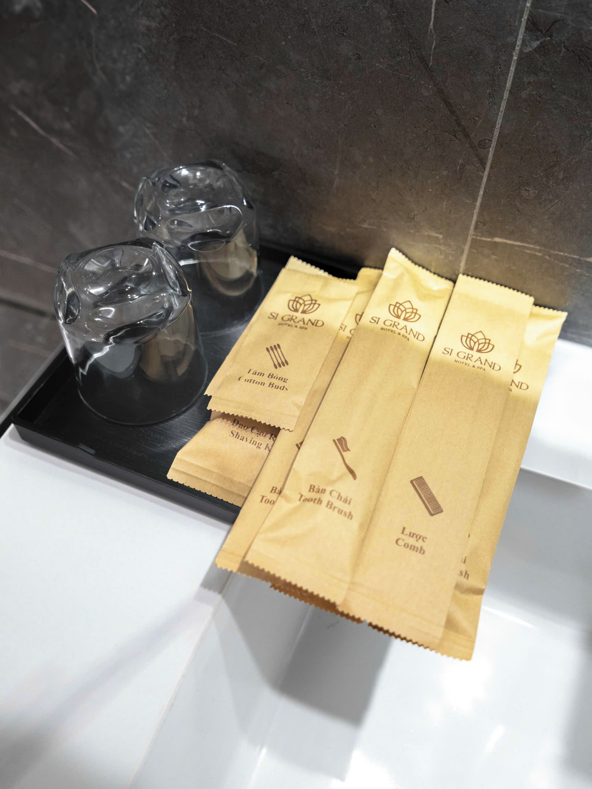 Une salle de bain avec un miroir, un récipient en verre et trois sacs en papier brun sur lesquels du texte est imprimé.