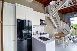 Eine Küche mit weißen Schränken, einem schwarzen Kühlschrank, einem Holzespeisetisch und einer Treppe.