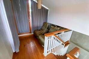 Una habitación con suelo de madera, una cuna blanca, un sofá con cojines y una puerta con cortinas.