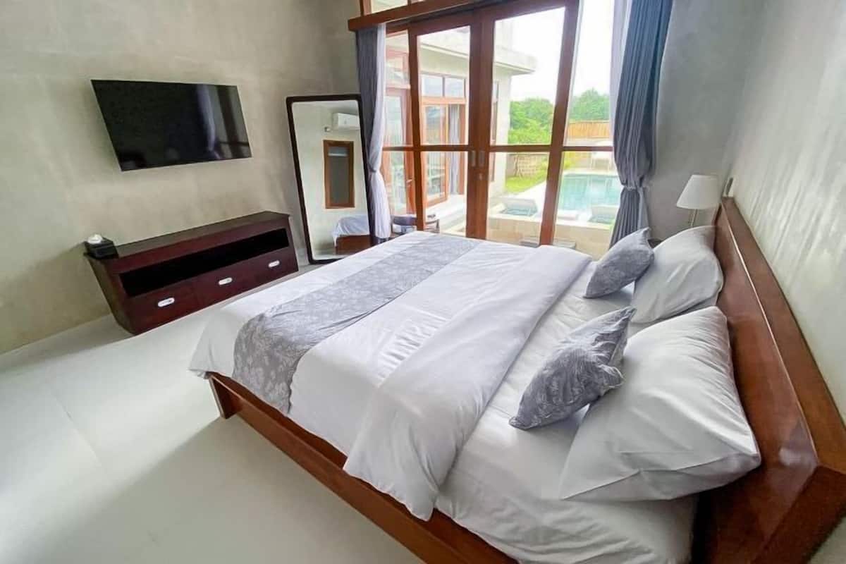 A bedroom with a large bed, a TV mounted on the wall, and a view of the outdoors through a sliding door.