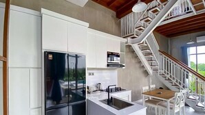 Une cuisine moderne avec des meubles blancs, un réfrigérateur noir et un coin repas comprenant des chaises blanches et une table en bois.